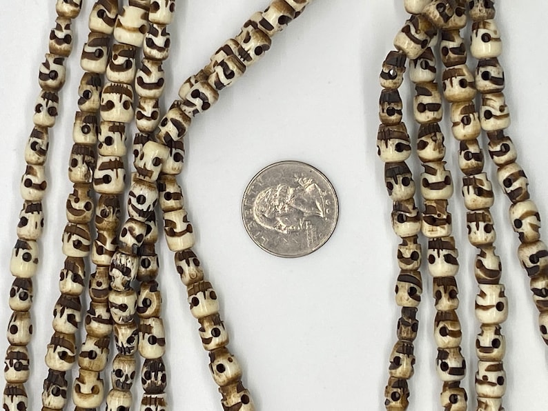 May include: A strand of white and brown skull beads with a carved design. The beads are approximately the size of a US quarter.