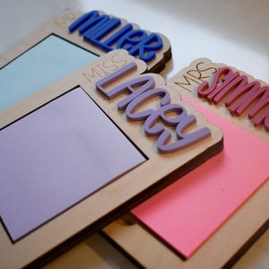 May include: Three wooden notepads with different colored sticky notes and names written on them. The names are "Miss Lacy", "Mr. Miller", and "Mrs. Simmons".