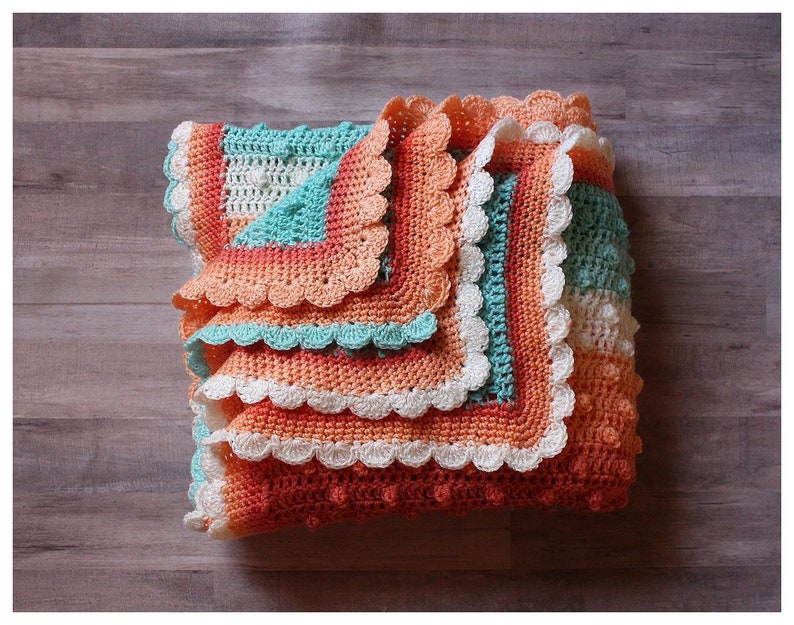 May include: A crocheted baby blanket with a scalloped edge in shades of peach, coral, white, and teal.