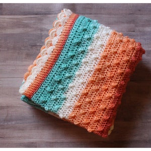 May include: A crocheted baby blanket with a textured stitch pattern. The blanket is made in shades of orange, white, and teal.