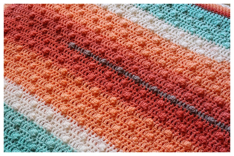 May include: A close-up of a crocheted blanket with a striped pattern in shades of coral, peach, white, and turquoise.