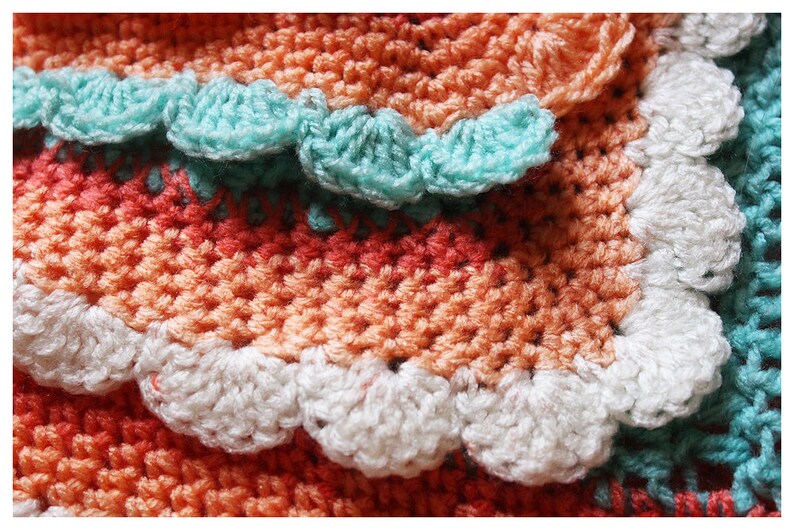 May include: A crocheted blanket with a multi-colored striped pattern and a scalloped edge. The blanket is made with different shades of orange, white, and turquoise yarn.