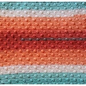 May include: A crocheted blanket with stripes of white, teal, and orange. The blanket has a textured pattern with small raised bumps.