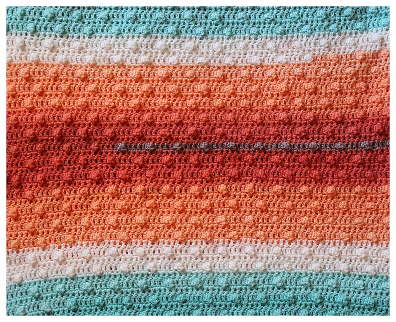 May include: A crocheted blanket with stripes of white, teal, and orange. The blanket has a textured pattern with small raised bumps.