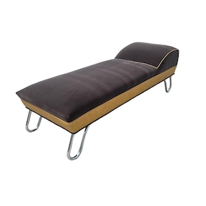 May include: A modern chaise lounge with a dark gray upholstered seat and backrest. The seat is trimmed with a tan border and gold piping. The legs are made of chrome-finished metal.