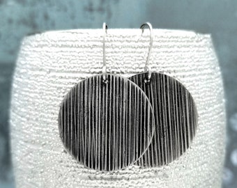 May include: A pair of silver earrings with a textured, striped design. The earrings are round and have a simple, minimalist style.