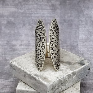 May include: A silver ring with a textured, hammered finish. The ring is open in the middle and has a unique, organic shape.