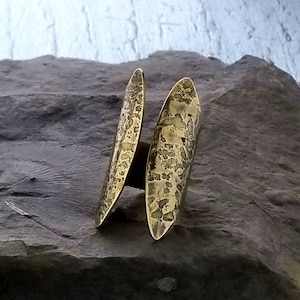 May include: A gold-toned ring with a hammered texture. The ring is made of two oval-shaped pieces that are joined together.