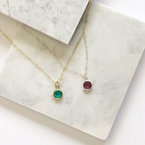 Pu&ograve; includere: Due delicate collane con pendenti rotondi con pietre preziose. Una presenta una catena dorata con un pendente turchese, l'altra una catena argentata con un pendente magenta. Entrambi i pendenti sono incastonati.