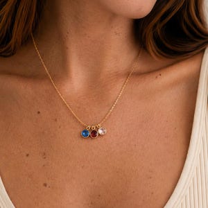 Pu&ograve; includere: Una collana dorata con tre piccoli pendenti rotondi blu, rossi e rosa. La collana &egrave; indossata su una canotta bianca a coste.