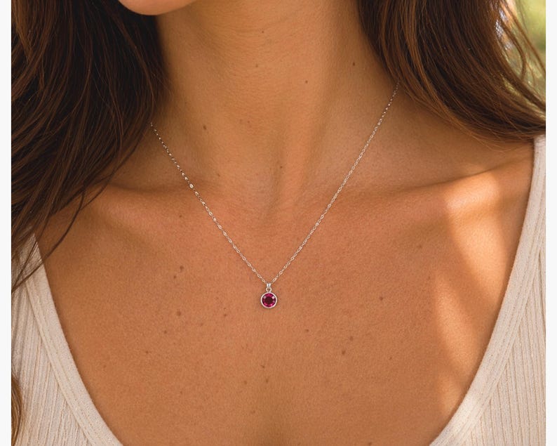 Pu&ograve; includere: Una delicata collana d'argento con un piccolo pendente rotondo color rubino. Il pendente &egrave; incastonato in una lunetta d'argento e appeso a una sottile catena. La collana &egrave; mostrata su uno sfondo neutro.