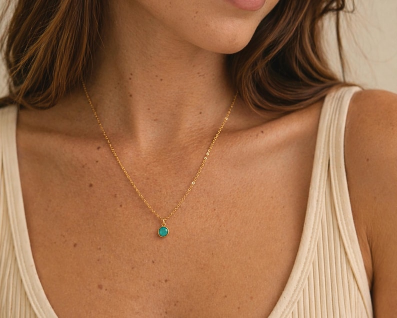Pu&ograve; includere: Una delicata collana d'oro con un piccolo pendente rotondo turchese. La collana &egrave; indossata, e la catena d'oro &egrave; visibile sulla pelle. Il pendente &egrave; di un vivace colore turchese.
