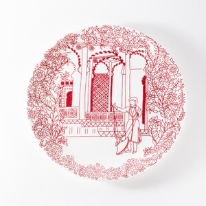 May include: A white ceramic plate with a red line drawing of an ornate building with a person standing in front of it. The building is surrounded by a border of red line drawings of flowers and leaves.