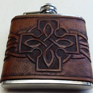 May include: A brown leather-wrapped stainless steel hip flask with a Celtic knot design. The flask has a silver cap and a silver base.