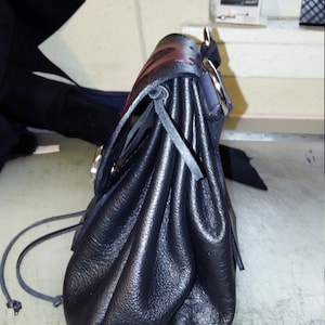 May include: A black leather bag with a drawstring closure and a red and black strap. The bag is folded and has a silver buckle.