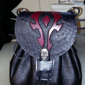 May include: A black leather bag with a red and black skull design. The bag has a drawstring closure and a skull-shaped buckle.