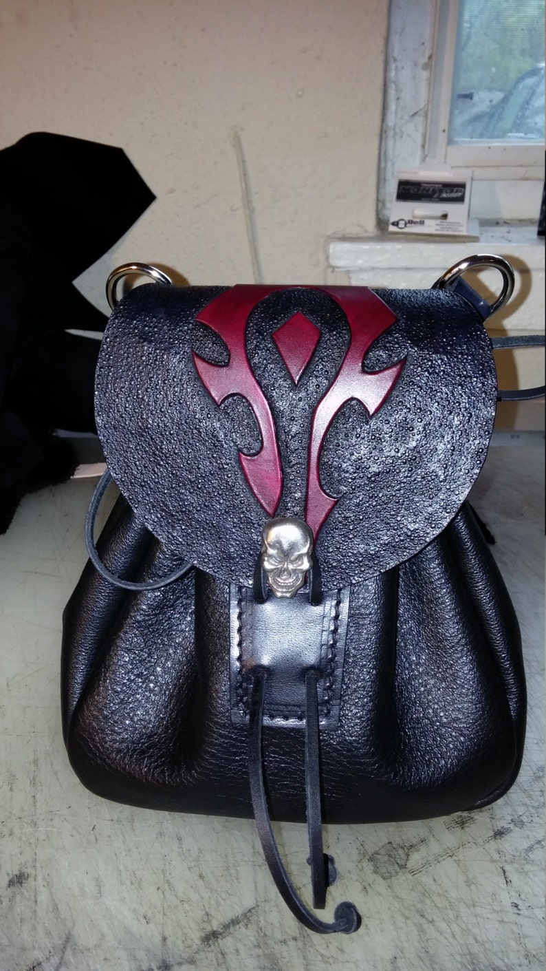 May include: A black leather bag with a red and black skull design. The bag has a drawstring closure and a skull-shaped buckle.