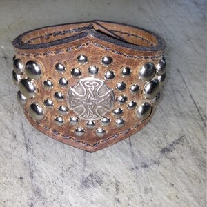 May include: Brown leather bracelet with silver studs and a Celtic cross design.