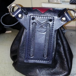 May include: Black leather pouch with a red and black flap. The pouch has a decorative stitched design and two metal rings.