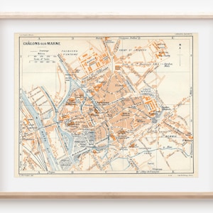 Op de afbeelding: Een vintage kaart van Châlons-sur-Marne, Frankrijk, gedrukt in zwarte, bruine en blauwe inkt op een crèmekleurige achtergrond. De kaart toont de straten, gebouwen en bezienswaardigheden van de stad, inclusief de Marne.