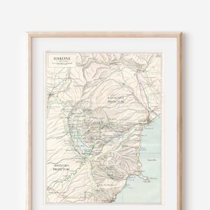 Puede incluir: Un mapa vintage de Hakone, Japón, que muestra las áreas circundantes de la prefectura de Kanagawa y la prefectura de Shizuoka. El mapa está impreso en tinta negra, marrón, verde y azul sobre un fondo crema.