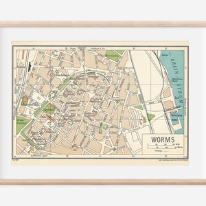 Könnte beinhalten: Eine Vintage-Karte von Worms, Deutschland, mit beigefarbenem Hintergrund und braunen Linien, die Straßen und Gebäude zeigen. Die Karte ist in einem hellen Holzrahmen gerahmt. Die Karte zeigt den Rhein und den Text "WORMS" in der rechten unteren Ecke.