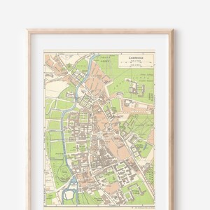 May include: Framed vintage map of Cambridge, featuring a detailed street layout with green, beige, and brown tones. The map includes the text "Cambridge" at the top. The map is encased in a light wooden frame.