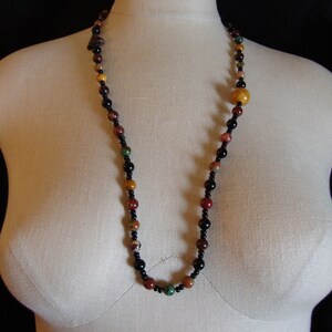 May include: A multi-colored beaded necklace with black, brown, yellow, red, and green beads. The necklace is on a white mannequin.