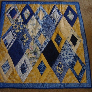 May include: A quilt with a diamond pattern in shades of blue, yellow, and white. The quilt is made of various fabrics with floral and geometric designs.