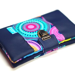 May include: A navy blue wallet with a colorful geometric pattern and a brass clasp. The wallet is folded closed and the clasp is closed.