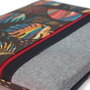 Könnte beinhalten: Eine schwarze Laptoptasche mit einem bunten tropischen Blättermuster und einem roten Reißverschluss. Die Tasche ist mit einem grauen Fleecefutter ausgestattet, um zusätzlichen Schutz zu bieten.
