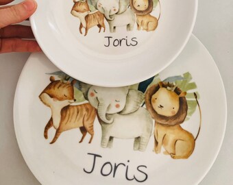 May include: Two white ceramic plates with a jungle animal theme. The plates feature a tiger, elephant, and lion with a crown. The name "Joris" is written on both plates.