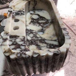 Peut inclure: Un évier rectangulaire en marbre avec un bord festonné. L'évier présente un motif marbré blanc et marron. Il possède un porte-savon intégré avec trois trous et un drain. L'évier est conçu pour une utilisation dans la salle de bain.