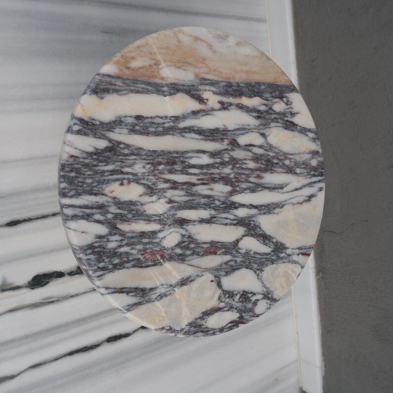 May include: A round, oval-shaped marble table top with a swirling pattern of white, grey, and pink.