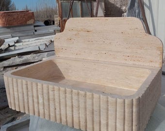 May include: A rectangular stone sink with a fluted edge and a backsplash. The sink is made of a light beige stone with brown veins.