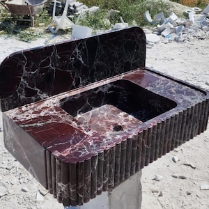 Può includere: Un lavabo da bagno in marmo rosso scuro con uno schienale e un bordo anteriore scanalato.