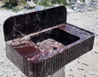 May include: A dark red marble bathroom sink with a backsplash and a fluted front edge.
