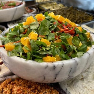 May include: A white marble bowl filled with a salad of fresh green lettuce, orange slices, and red pepper pieces.