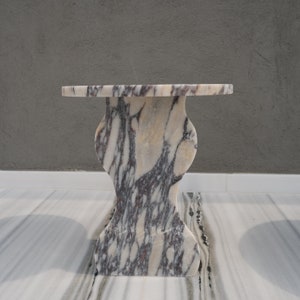 May include: A white marble side table with a unique, organic shape and a swirling pattern of grey and purple veins.
