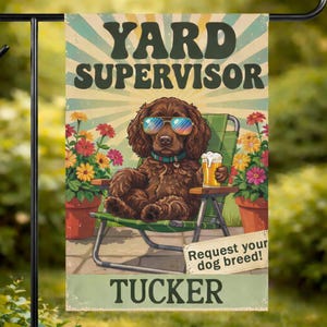 Op de afbeelding: Een tuinvaandel met de tekst "YARD SUPERVISOR" en de naam "TUCKER". De vlag toont een bruine hond met een zonnebril en een biertje, zittend in een groene stoel. Kleurrijke bloemen staan in potten aan weerszijden.
