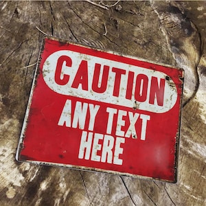 Puede incluir: Un letrero de metal rojo con texto blanco que dice "CAUTION ANY TEXT HERE". El letrero tiene un aspecto desgastado y vintage.