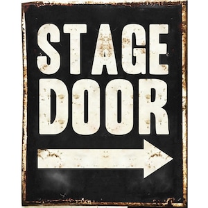 Puede incluir: Un letrero de metal blanco y negro con las palabras "Stage Door" y una flecha blanca apuntando hacia la derecha. El letrero tiene un aspecto desgastado y oxidado.