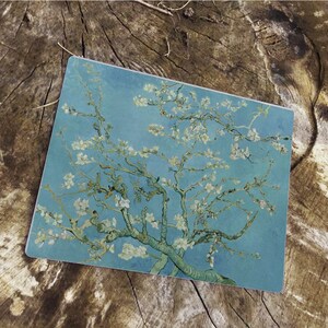 Puede incluir: Una pintura de un almendro en flor con flores blancas sobre un fondo de cielo azul. Las ramas del árbol están representadas en un estilo arremolinado y expresivo, característico de la obra del artista.