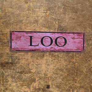 May include: A pink and black metal sign with the word "LOO" printed on it.