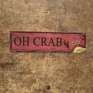 Puede incluir: Un letrero de metal rojo y negro con el texto "OH CRAB" y un cangrejo de dibujos animados con ojos grandes.