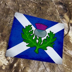 Puede incluir: Una bandera escocesa azul y blanca con un cardo verde en el centro. La bandera tiene un aspecto desgastado y vintage.