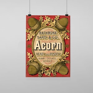 Puede incluir: Anuncio vintage para estufas y cocinas Acorn de Rathbone, Sard & Co. La imagen presenta un fondo rojo con un marco ovalado dorado que contiene el nombre de la empresa y la información del producto. El marco está rodeado de hojas de roble y bellotas estilizadas.
