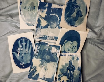 May include: A collection of six rectangular paper prints featuring blue-toned monochromatic imagery. The prints display various portraits of individuals, a hand with the text ARMY, and abstract shapes, all rendered in a textured, ink-washed style.
