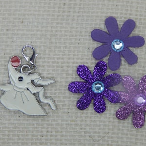 May include: A white metal charm of the character Zero from the movie The Nightmare Before Christmas. Zero is holding a red ball in his mouth and is wearing a white dress. The charm is attached to a silver metal ring. The charm is surrounded by three purple glitter flowers with blue glitter centers.