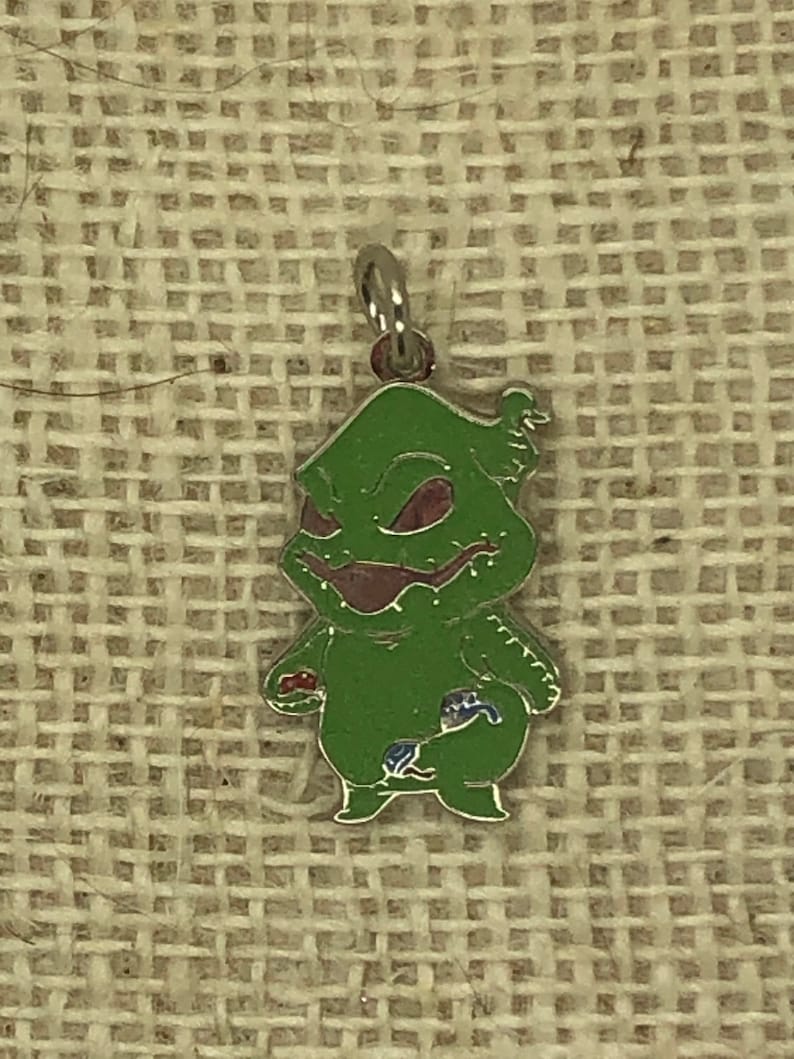 May include: A green, enamel charm of a character from the movie The Nightmare Before Christmas. The character is wearing a red and blue outfit and has a mischievous grin.